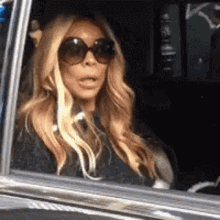 a woman wearing sunglasses is sitting in a car with her mouth open .