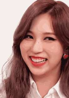 a woman wearing a white shirt and red earrings smiles