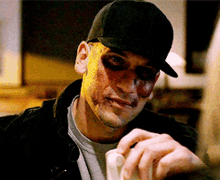 a man with yellow paint on his face is wearing a baseball cap and a black jacket