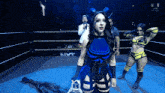 a woman in a blue and black outfit stands in a wrestling ring with the word nxt on the wall behind her