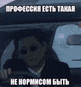 a man in a suit and sunglasses is driving a car with a meme in russian