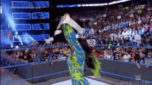 a woman in a blue and green outfit is doing a handstand on a wrestling ring