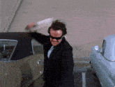 a man wearing sunglasses and a suit is standing in front of a car