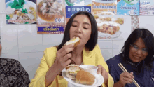 a woman in a yellow jacket is eating a sandwich in front of a sign that says 60