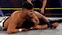 two men are wrestling in a wrestling ring and one of them is laying on the floor .