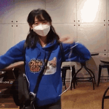 a girl wearing a mask and a blue hoodie with a cat on it is dancing .