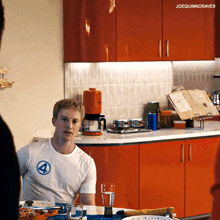 a man in a white shirt with the number 4 on it sits in a kitchen