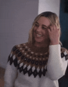 a woman wearing a brown and white sweater is smiling and touching her hair