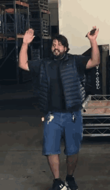a man in a black shirt and blue shorts is standing in a warehouse with his arms in the air