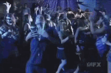 a man in a blue shirt is dancing in front of a group of people with avfx written on the bottom