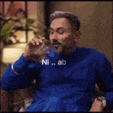 a man in a blue shirt is drinking from a glass with the words ni ab below him