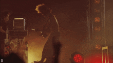 a man playing a guitar in a dark room with the letter d visible