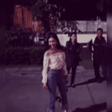a woman is walking down a sidewalk with a skateboard while a group of people are standing behind her .