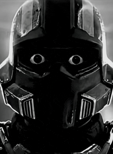 a black and white photo of a robot wearing a helmet with a mask on his face .