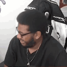 a man with a beard and glasses is wearing a black shirt and a gold chain .
