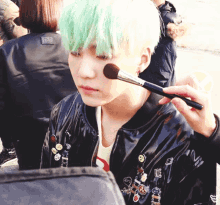 a person applying makeup to a young man with green hair