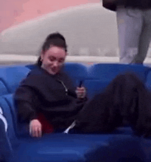 a woman is sitting on a blue couch with her legs crossed and looking at her phone .