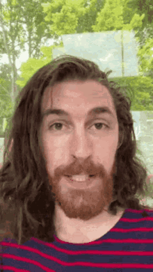 a man with long hair and a beard is smiling for the camera .
