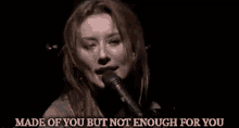 a woman is singing into a microphone with the words `` made of you but not enough for you '' behind her .
