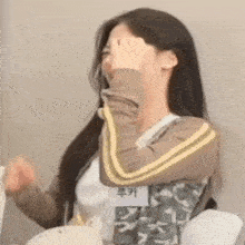 a young woman is covering her face with her hand while sitting at a table .