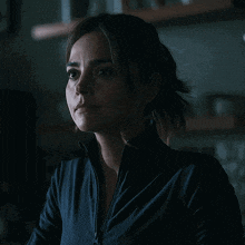 a woman in a dark room with a ponytail is wearing a black jacket