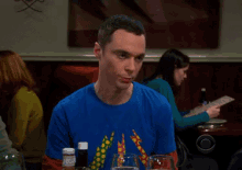 a man wearing a blue shirt with a giraffe on it sits at a table