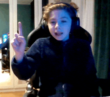 a young boy wearing headphones is sitting in a chair and giving the middle finger