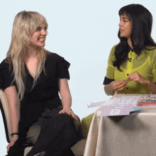 two women are sitting at a table and one of them is wearing a green shirt
