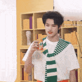 a man wearing a green and white striped scarf is holding a can of orange juice