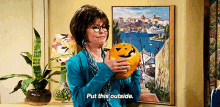 a woman is holding a pumpkin and says put this outside