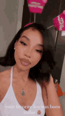 a woman in a white tank top is taking a selfie with a pink headband on her head .