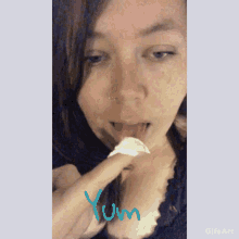 a close up of a woman licking a piece of paper with the word yum written below her