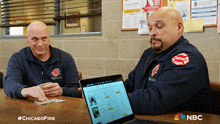 two firefighters sitting at a table with a laptop and a chicago fire logo on their jackets