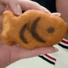 a person is holding a fish shaped pastry with a smiley face on it .
