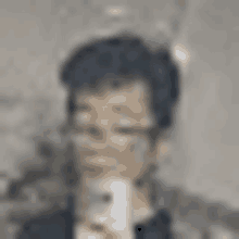 a blurry picture of a man wearing glasses and a suit holding a cell phone .