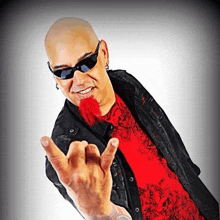 a bald man with a red beard wearing sunglasses and a red shirt is making a rock sign .