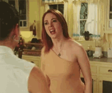 a woman in a tan one shoulder top is standing next to a man in a kitchen