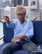 a man in a blue shirt is pointing at the camera while sitting on a blue couch ..