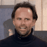 a man with a beard is wearing a black turtleneck sweater and smiling