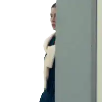 a woman in a striped dress stands behind a gray wall