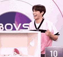 a man in a pink shirt is standing in front of a box with the word boys on it .