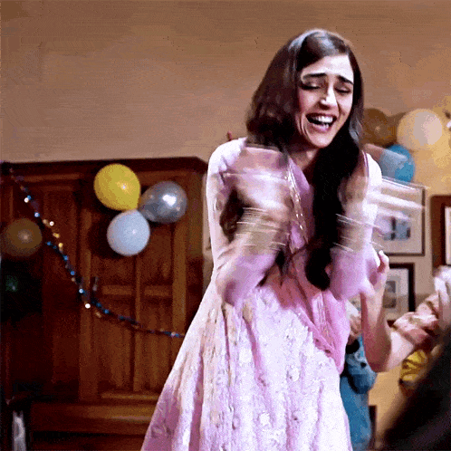 a woman in a pink dress is standing in a room with balloons 
