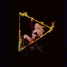 a woman in a black bra is holding a triangle with fire coming out of it