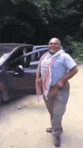 a man in a blue shirt is standing in front of a car .