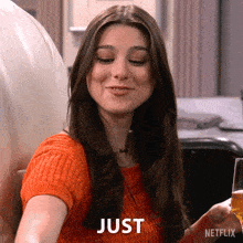 a woman is holding a glass of wine and smiling with just written on her face