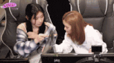 two women are sitting in front of a computer screen with ah written on the bottom right