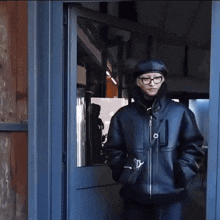 a man wearing glasses and a hat is standing in a doorway .