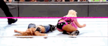 two women are wrestling in a wrestling ring and one is laying on the ground .