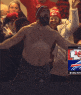 a shirtless man stands in a crowd of people with a cbs advertisement in the background