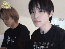 a man wearing a black t-shirt with chinese writing on it is standing next to another man